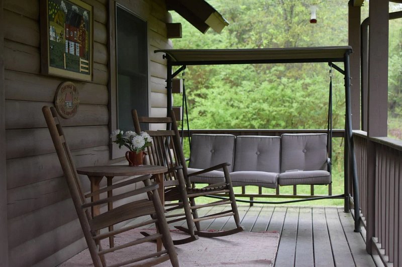 Wooden rocking chairs and a cushioned swing on a shaded country porch