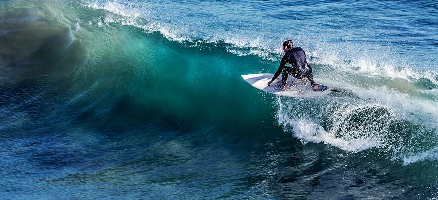 A longboarder holding trim across a clean green wall at First Point, Malibu.