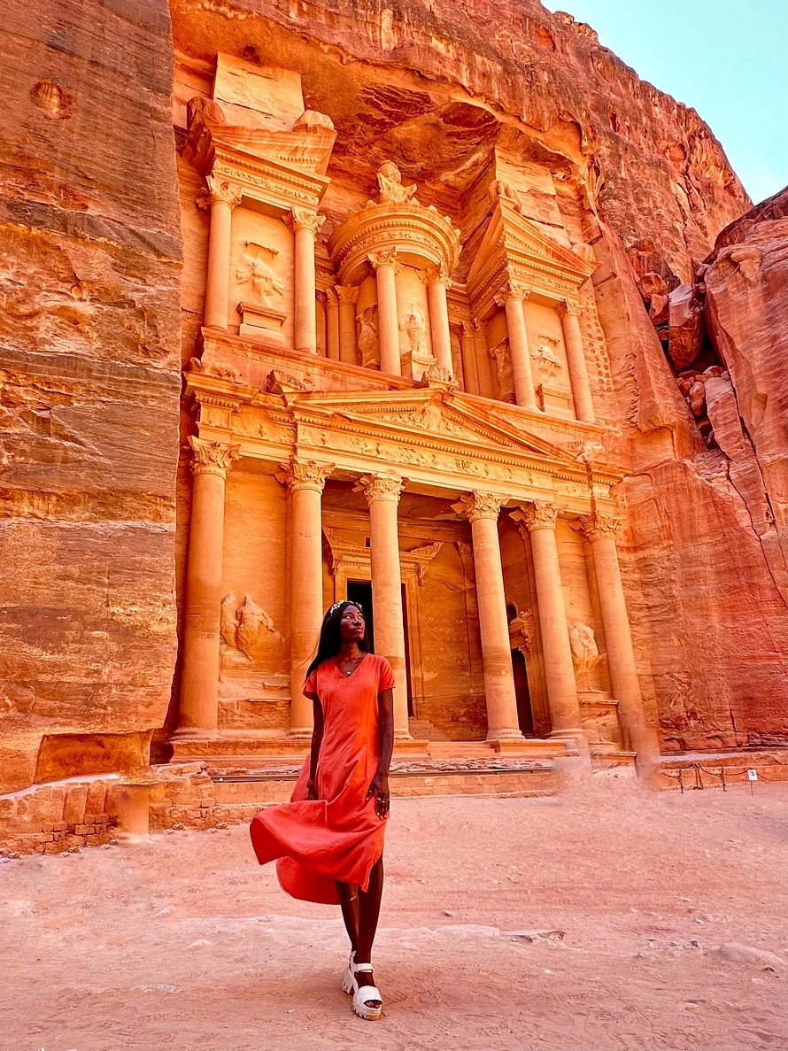 Maacah wears a burnt orange silk dress in front of the Treasury in Petra, Jordan.