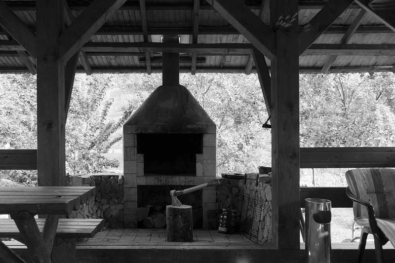 A rustic covered outdoor gathering space with timber beams, a picnic table, and a masonry barbecue, photographed in black and white