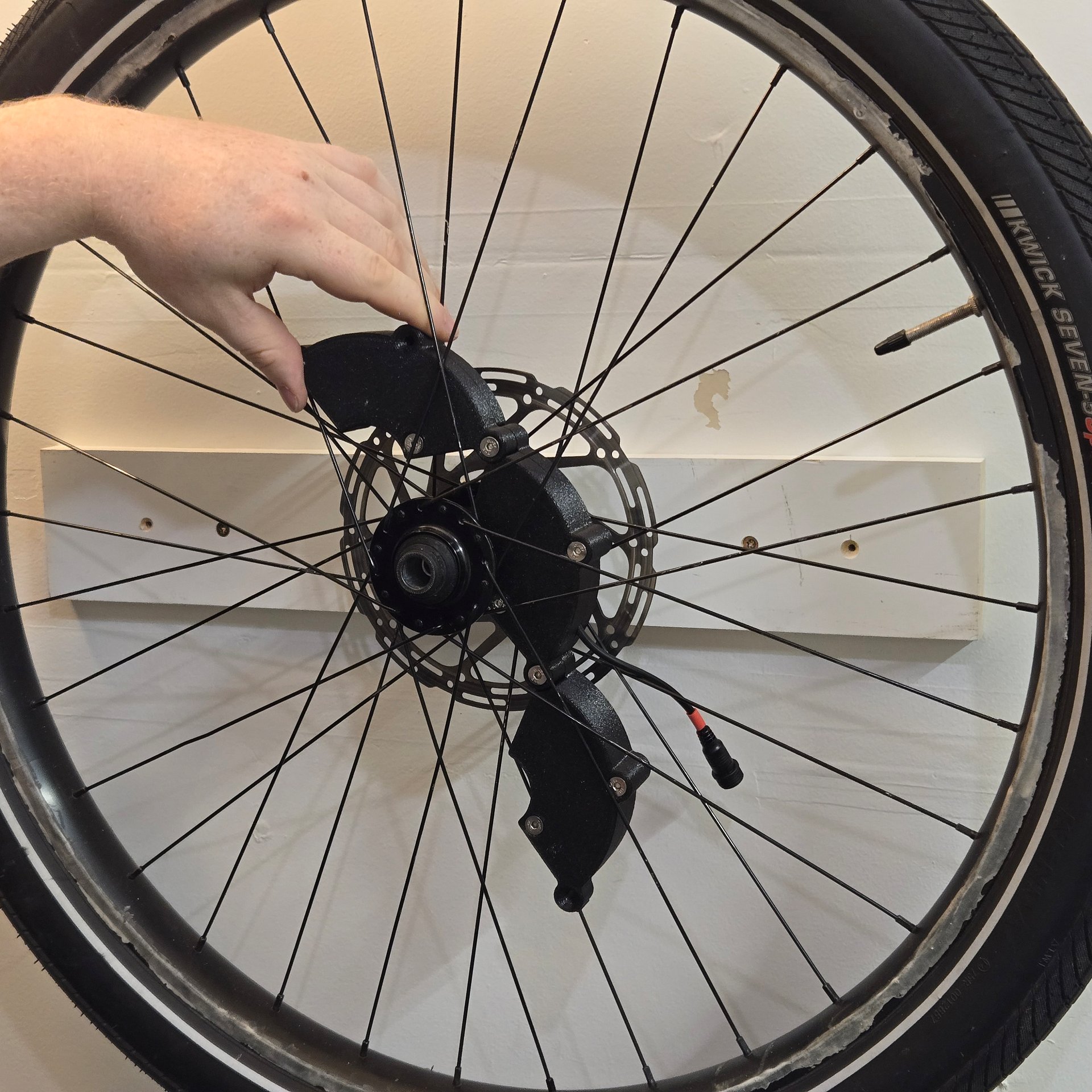 An three-part hinged rechargeable 12V battery case, unfolded and being installed in a bike wheel around the hub.