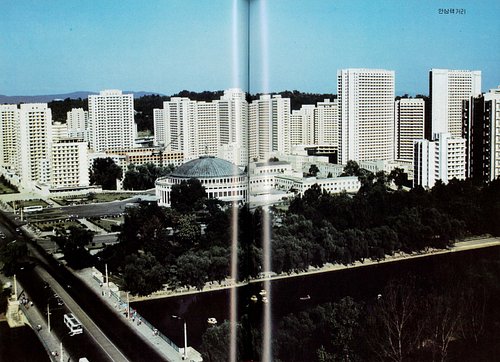 An archival view of An Sang Thaek Street in Pyongyang, with rows of apartment towers overlooking a tree-lined riverbank. Repe...