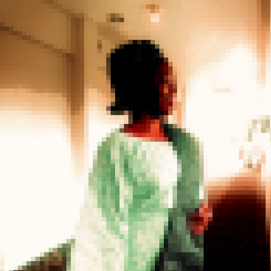 A pixlated picture of a Nigerian women wear green traditional wear looking away from the camera in a white hall way with dark carpet.