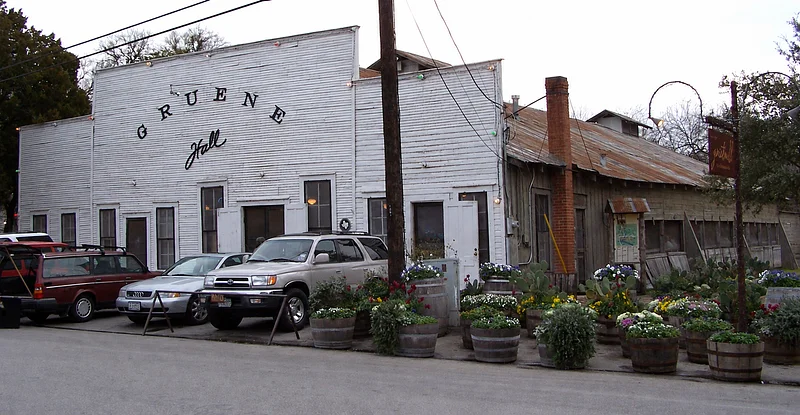 Historic Gruene Hall exterior with parked cars and flower barrels