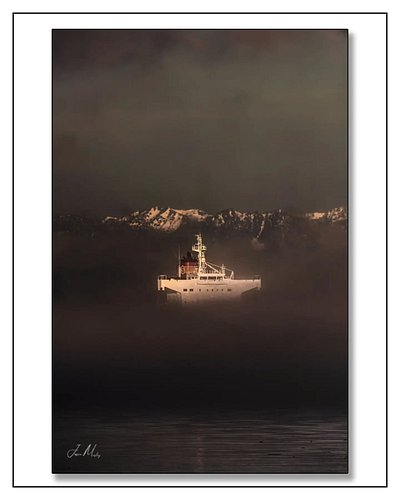 Evening light breaks through the fog in Elliott Bay — a ship at anchor glowing against the dark, Olympic peaks rising above t...
