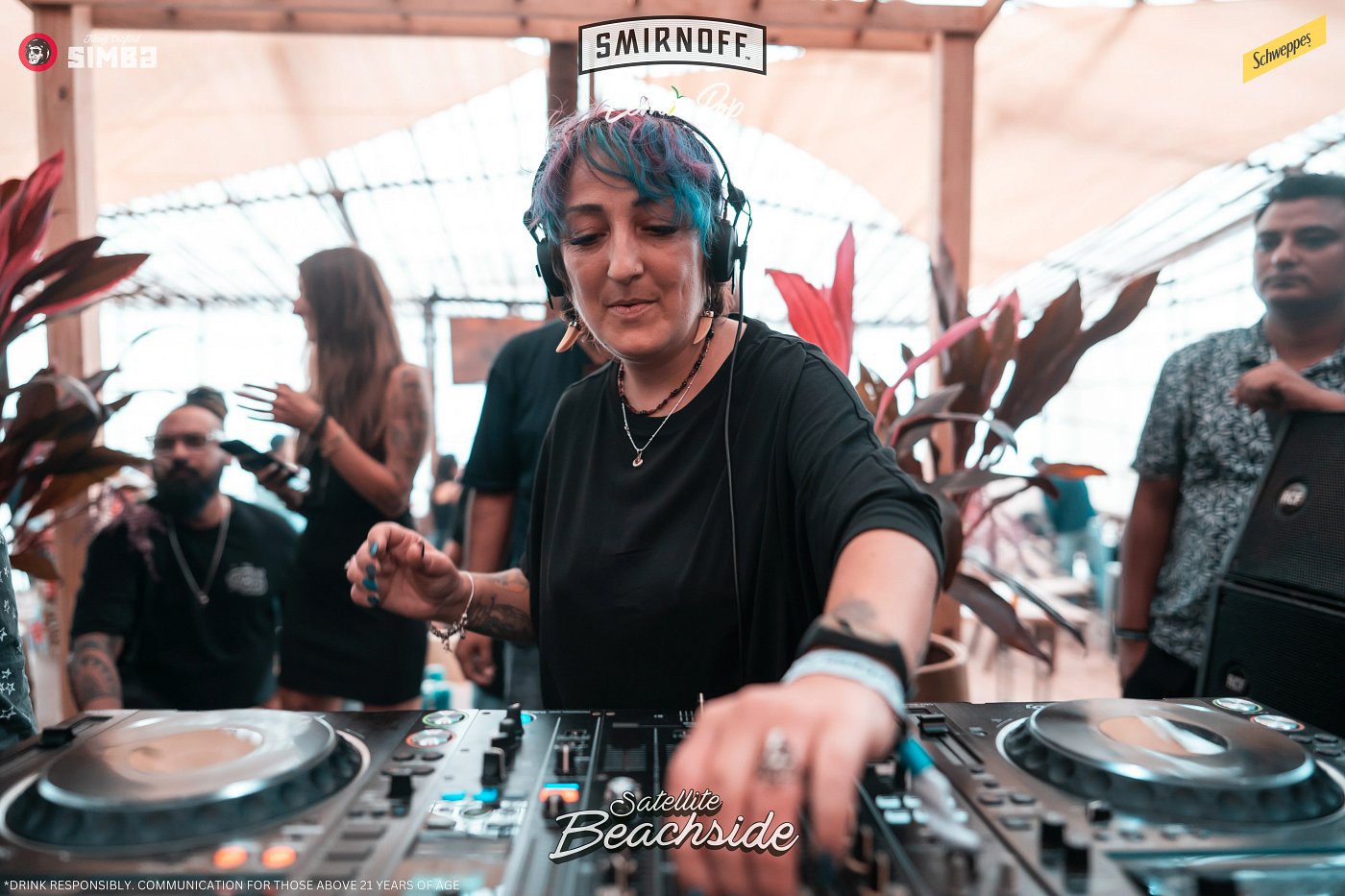 Liora-Nehama with turquoise hair and headphones, adjusting the DJ mixer during a daytime set.