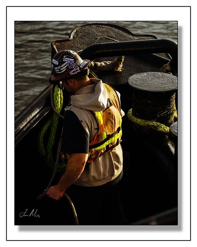 Hard work on the water. A deckhand works the lines on a tugboat in Puget Sound — safety vest on, ropes in hand, getting it do...