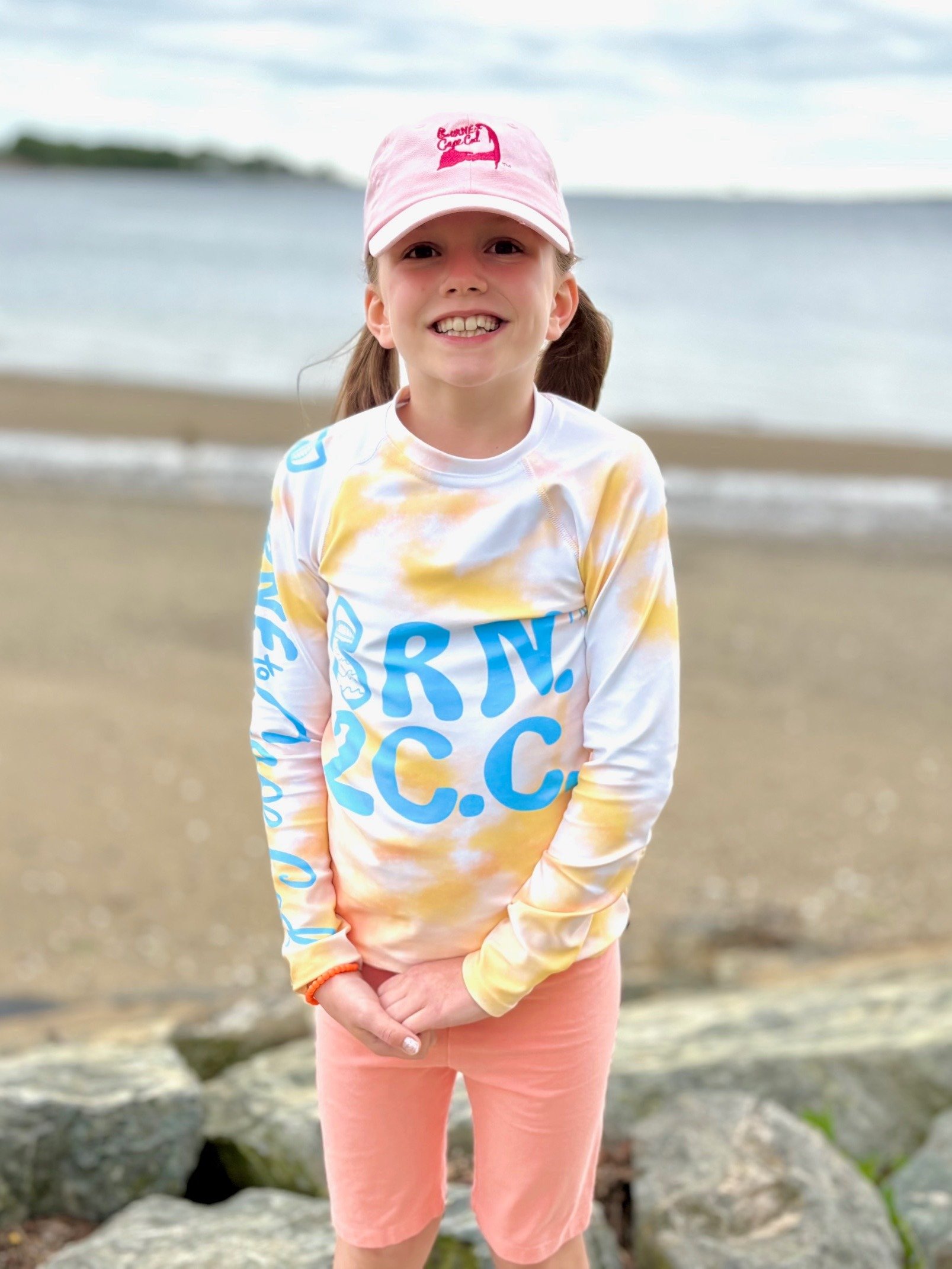 YOUTH | Rash Guard | BRN.2C.C.™ Front Graphic | BOURNE to Cape Cod™ Sleeve & Back Logo | Coastal Swim Shirt for Kids | UV Protection Activewear | Blue Logo on Orange Tie-Dye product image (4)